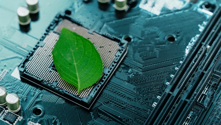 Green leaf on a semiconductor circuit board chip, suggesting environment and business sustainability.